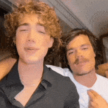 two men with curly hair and mustaches are posing for a photo