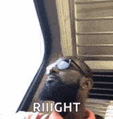 a man with a beard and sunglasses is sitting on a train looking out the window .