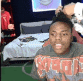 a man wearing a shirt that says raptors is sitting in front of a bed .