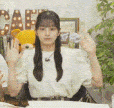 a girl is sitting at a table with a teddy bear in the background and waving at the camera .