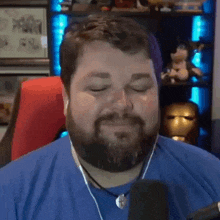 a man with a beard wearing headphones and a blue shirt is sitting in front of a microphone .