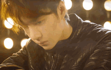 a young man wearing a black leather jacket looks down