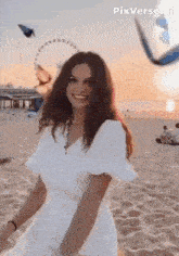a woman in a white dress is standing on a beach at sunset .