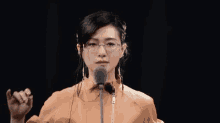a woman wearing glasses stands in front of a microphone with chinese writing on the bottom