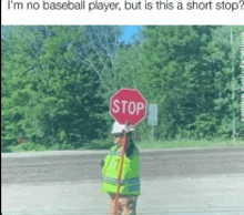 a man in a yellow vest is standing next to a stop sign .