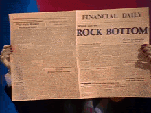 a person is holding a financial daily newspaper with the headline rock bottom