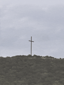 a large wooden cross on top of a hill with trees in the background