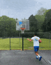 a man in a white shirt with a whale on the back is playing basketball in a park