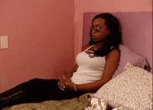 a woman is sitting on a bed with a pink wall behind her