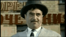 a man wearing a hat and tie is standing in front of a building that says pie