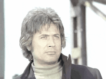 a man wearing a turtleneck and a black jacket looks to the side