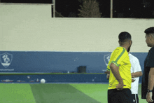 a man in a yellow shirt stands on a soccer field with other men