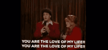 a man and a woman are standing on a stage and the man is saying you are the love of my life .