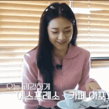 a woman in a pink jacket sits at a table with two cups and saucers