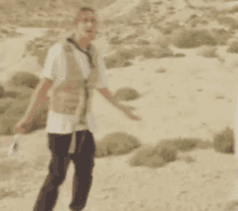 a man in a vest is standing in a desert holding a camera .