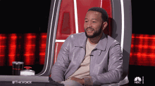 a man in a purple leather jacket is sitting in a chair with a nbc logo behind him