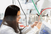 a woman in a lab coat and goggles works on a device