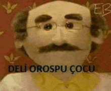 a puppet with glasses and a mustache is wearing a yellow shirt and a yellow tie .