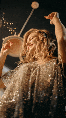 a woman in a sequined dress is dancing with her arms up