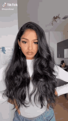 a woman with long black hair is wearing a white top and jeans
