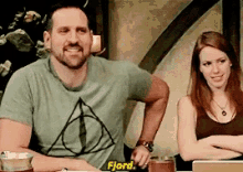 a man and a woman are sitting at a table and the man is wearing a fjord shirt