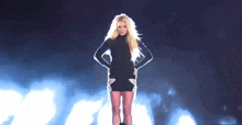 a blonde woman in a black dress is standing on a stage with her hands on her hips