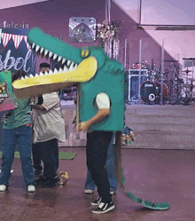 a man in a crocodile costume stands in front of a drum set that says tama