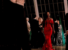 a woman in a red dress is walking in front of a man in a black suit