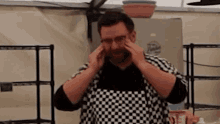 a man wearing glasses and an apron is covering his ears with his hands .