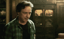 a man in a green plaid shirt and black shirt is standing in a dark room .
