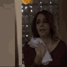 a woman in a red shirt is holding a white towel over her mouth .
