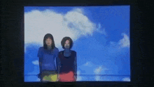 two women are standing next to each other in front of a blue sky on a television screen .