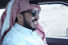 a man wearing sunglasses and a head scarf is sitting in a car .