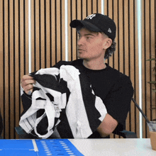 a man wearing a new york yankees hat holds a black and white shirt