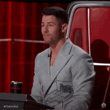 a man in a suit is sitting in front of a microphone on a red chair .