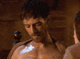 a shirtless man with a beard and a towel around his neck looks at a woman