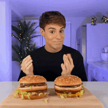 a man sitting at a table with two hamburgers in front of him