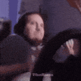 a woman is sitting in a chair holding a steering wheel and making a funny face .