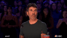 a man in a black shirt is sitting in front of a crowd with a cup of soda in his hand