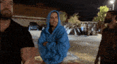 a man in a blue hoodie is standing with his arms crossed in a parking lot