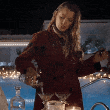 a woman in a red coat pouring a drink into a martini glass