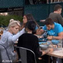 a group of people are sitting at a table with a man wearing a blue shirt that says ' calvin klein ' on it