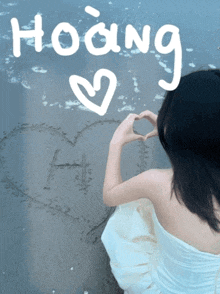a woman is making a heart shape with her hands and the word hoàng is written in the sand