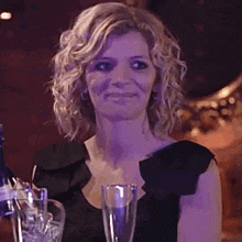 a woman is covering her mouth with her hand while sitting at a table with a glass of wine and a bottle of champagne .