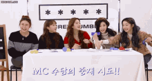 a group of girls are sitting around a table with a sign that says mc