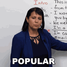 a woman in a blue jacket stands in front of a white board with the word popular on it