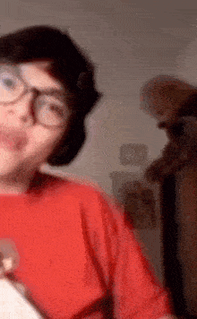 a person wearing glasses and a red shirt is standing in a room .