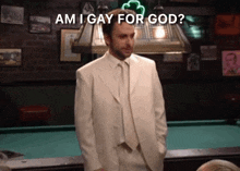 a man in a white suit stands in front of a pool table with the words am i gay for god written above him