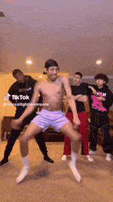 a group of young men are dancing in a living room with a man without a shirt dancing in the middle