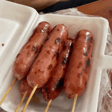 a styrofoam container filled with grilled sausages on sticks